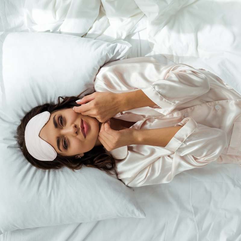 Woman relaxing in bed wearing satin sleepwear, showing the smooth feel and luxurious fabric of satin