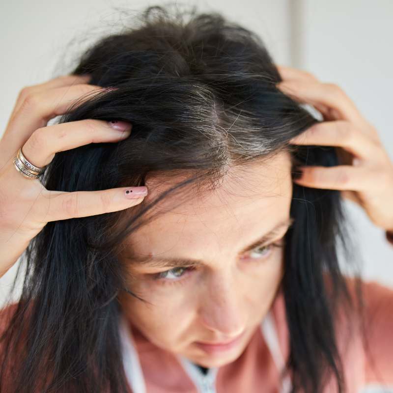 Woman inspecting scalp for thinning hair and gray strands after stressful event